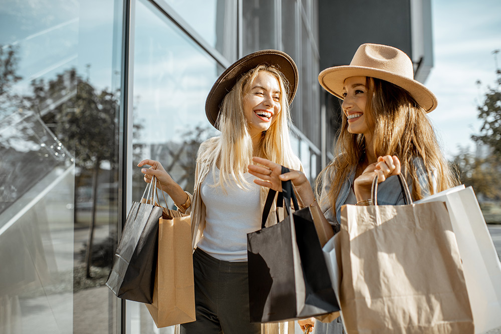 Two women wearing hats and holding shopping bags while walking and smiling outside a store with glass windows, just after discovering the best loyalty program app for small businesses. Two women wearing hats and holding shopping bags while walking and smiling outside a store with glass windows, just after discovering the best loyalty program app for small businesses.